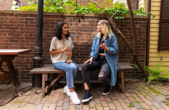 2 women sitting on brown wooden bench